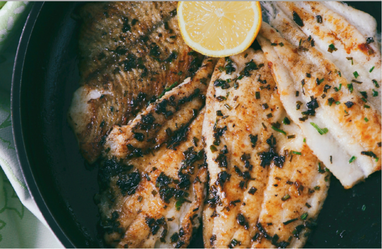 seared halibut fillets in a pan with a slice of lemon on top.
