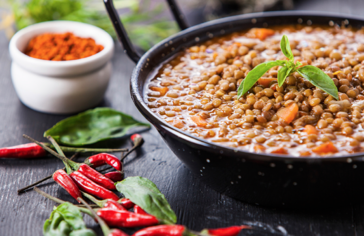 a bowl of lentil soup garnished with green herb beside red bird-eye chilies and a small bowl of sweet paprika on a wooden table