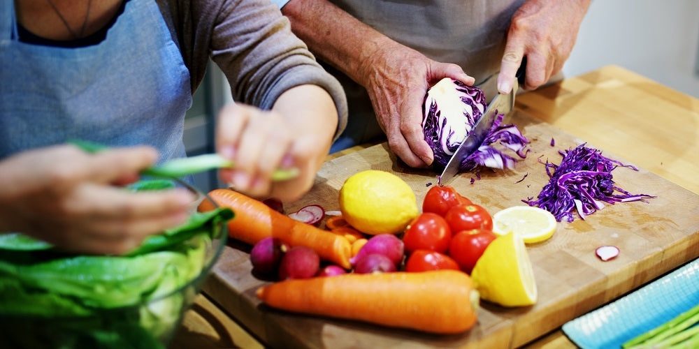 2 people slicing some vegetables on a wooden chopping board.