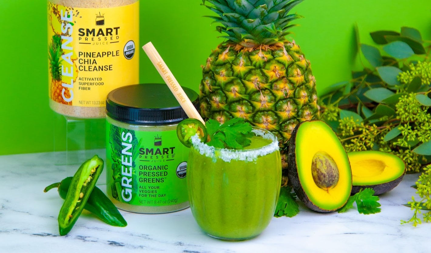 Green background with a green smoothie in a glass, Pineapples, Avocado, and Jalapenos are behind it