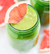 A close up shot of a green smoothie in a mason jar with a wedge of pink grapefruit on the side