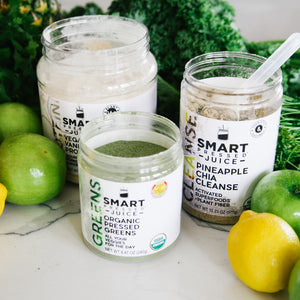 One 500 grams open jar of Vegan Vanilla Proteini, in front is one 240 grams open jar of Organic Pressed Greens beside one 375 grams open jar of Pineapple Chia Cleanse surrounded by green vegetables, 1 lemon, and green apples.