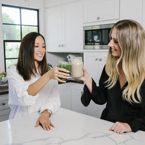 Two beautiful and healthy-looking ladies, each holding a jar of smoothies making a toast.