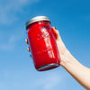 A woman's hand holding a jar of red smoothie held up against the blue sky.