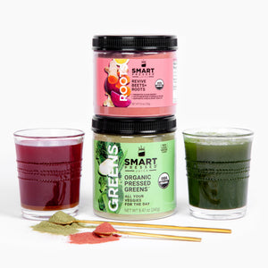 A glass with a purple juice beside a jar of 150 grams Revive Beet+Roots stacked in a jar of 240 grams Organic Pressed Greens, and beside is a glass with a green juice. In front is 2 stirring spoons full of green and dark pink powder. Set against a white background.